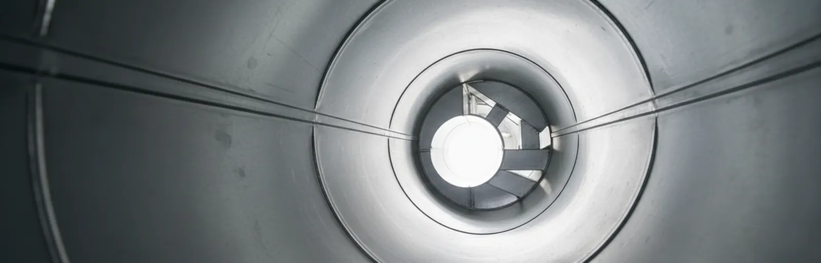 Looking down a clean, round metal air duct toward the register opening