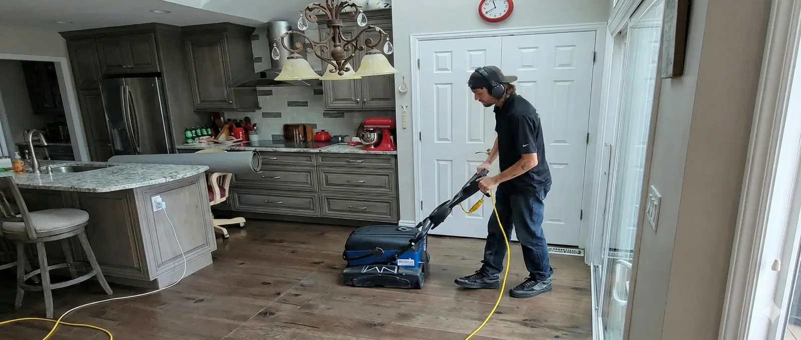Jake running a floor cleaning machine across the hardwood of an open kitchen and living area