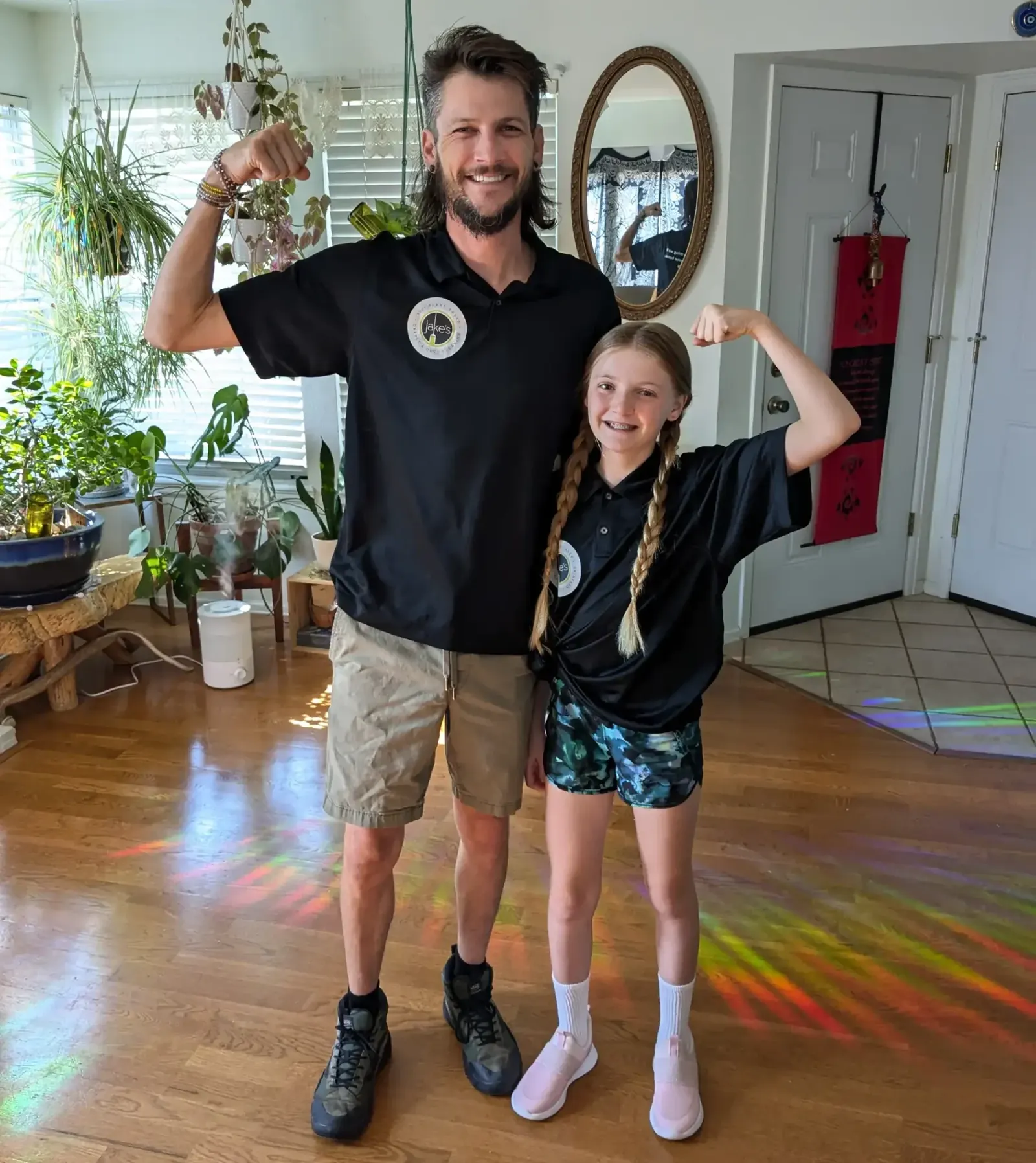 Jake and his daughter flexing their arms on a sunlit hardwood floor