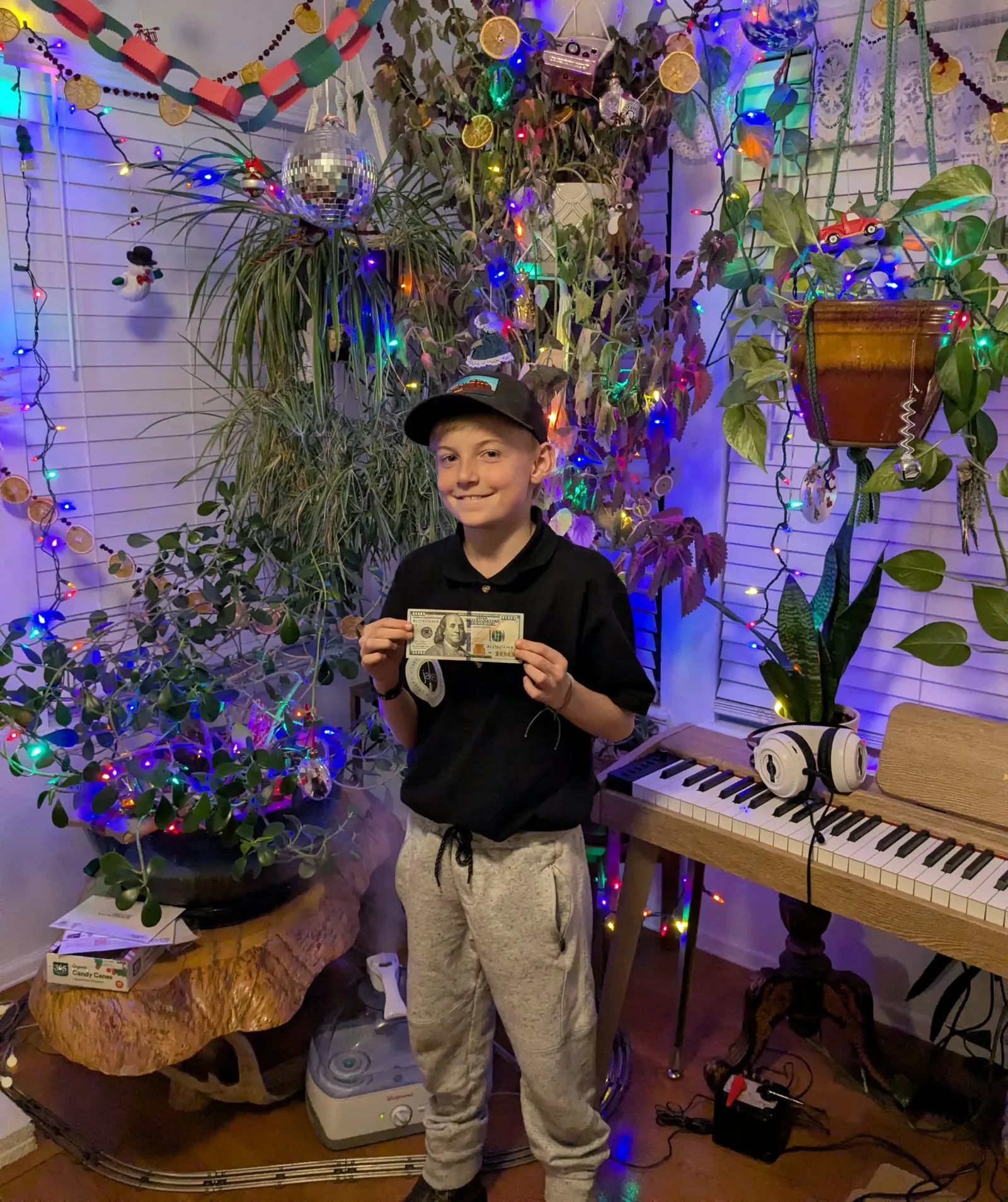 Jake's son holding up a dollar bill in a room full of plants and holiday lights