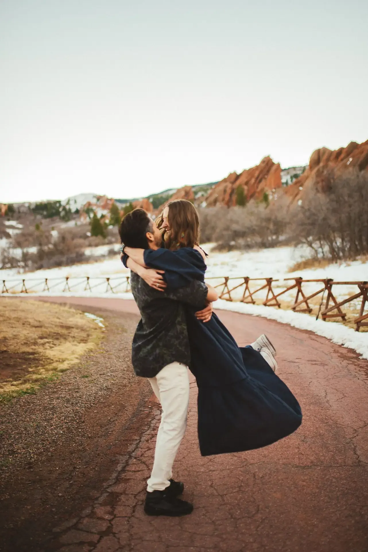 Jake lifting his wife in a hug on a trail among red rock formations