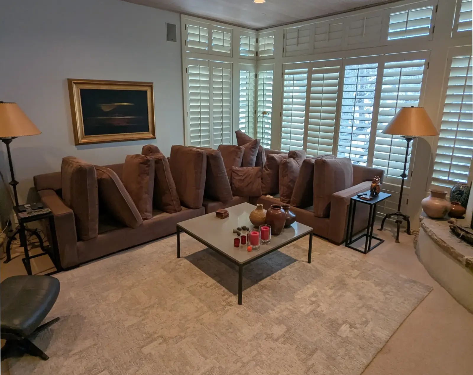A freshly cleaned living room with a light carpet, leather sofas and plantation shutters