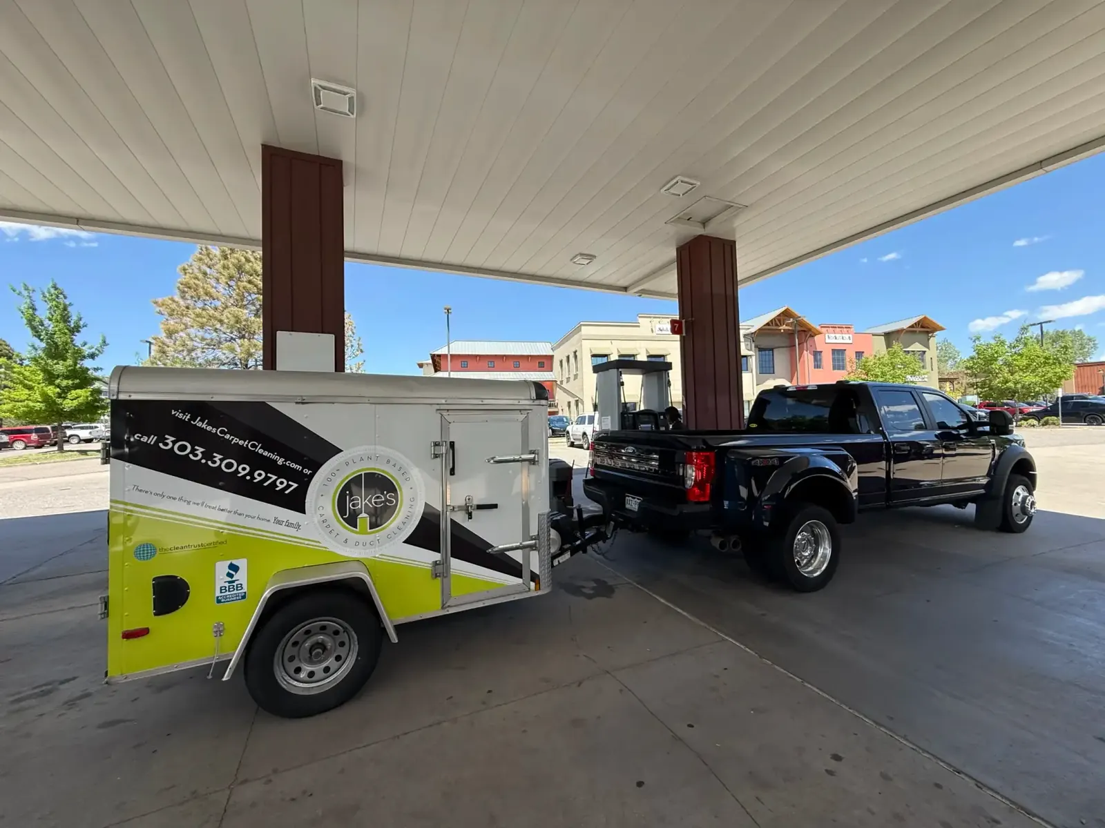 Jake's pickup and lime green branded trailer parked under a gas station canopy